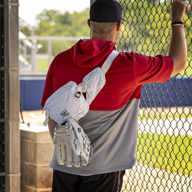 A player standing in a dugout with a white Rawlings sling bag on his back - SKU: RSLINGBG