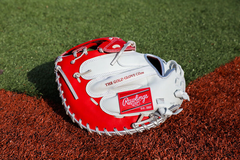 A white/scarlet Liberty Advanced Color Series catcher's mitt with a red Rawlings patch on a field - SKU: RLACM34FPWSP
