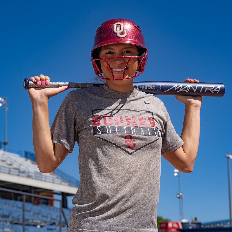 A picture of Jayda Coleman holding a 2025 Mantra fastpitch bat behind her neck