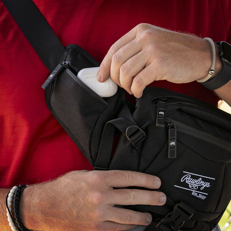A player putting an ear bud case in the side pocket of a black Rawlings sling bag - SKU: RSLINGBG