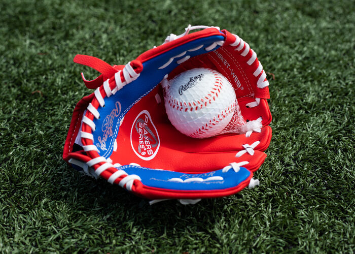 A baseball in the palm of a Rawlings Player Series youth glove lying on a field - SKU: PL91SR