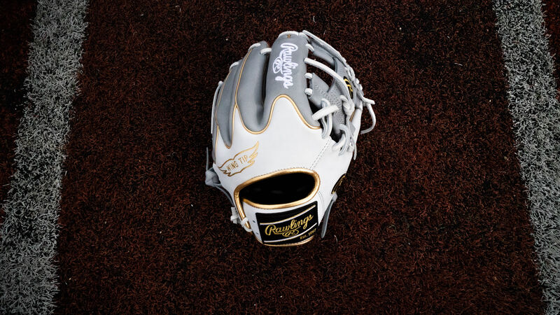 A white/grey Rawlings exclusive Heart of the Hide Wing Tip glove laying in the batters box on a field - SKU: PRO204W-2GW
