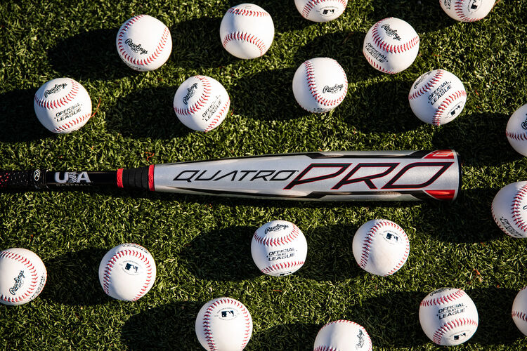 A gray Rawlings Quatro Pro youth bat on a field with baseballs around it - SKU: US1Q8