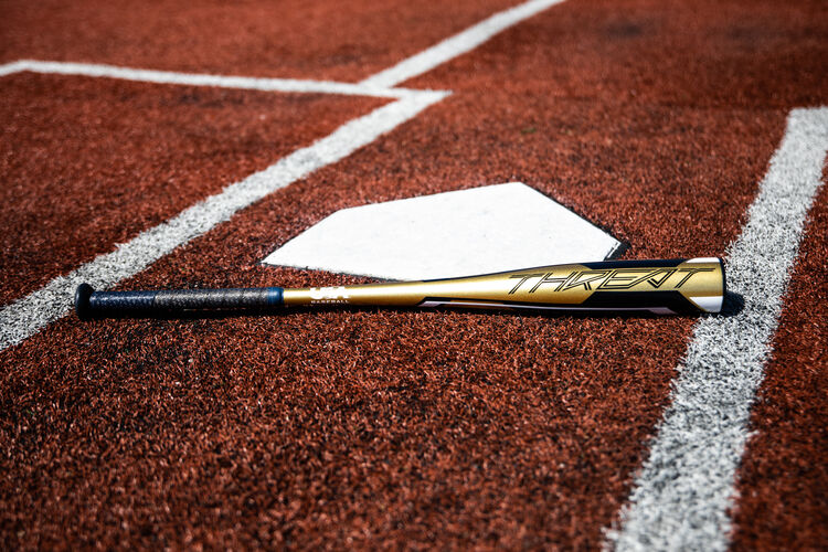 A gold Rawlings 2020 USA Threat bat lying on a field next to home plate - USZT12