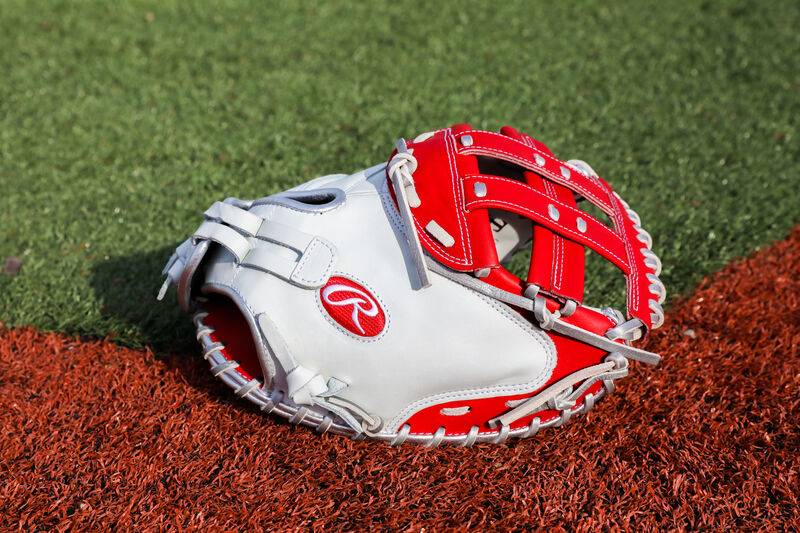 A white/scarlet Liberty Advanced Color Series 34-Inch catcher's mitt with on a field - SKU: RLACM34FPWSP