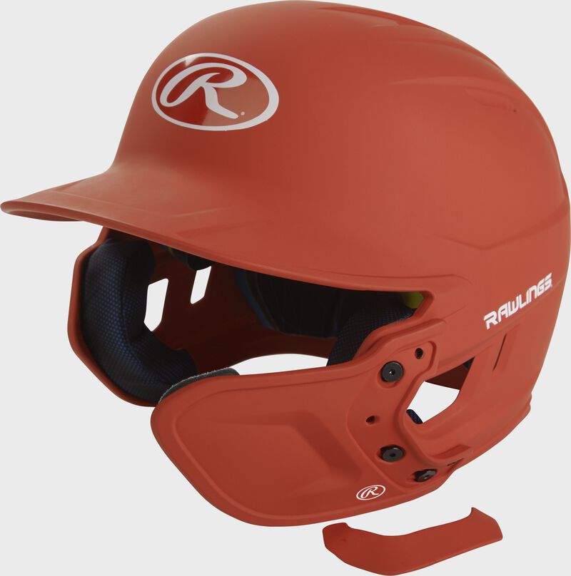 A burnt orange MEXTR attached to a Mach batting helmet with the removable TPU piece off to show the hardware