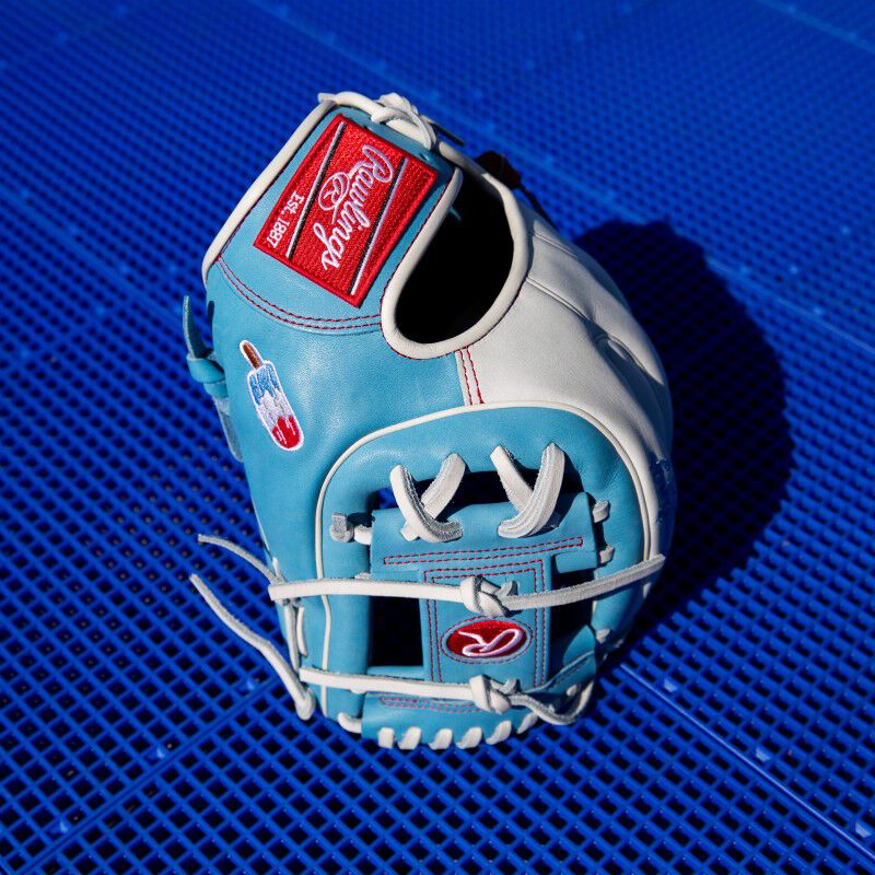 A Heart of the Hide Fro-Glo glove standing on it's finger tips with a blue background