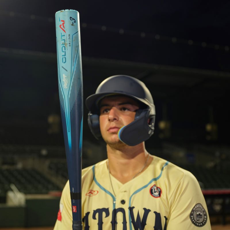 A player on a field holding and looking at the barrel of a Clout AI BBCOR bat