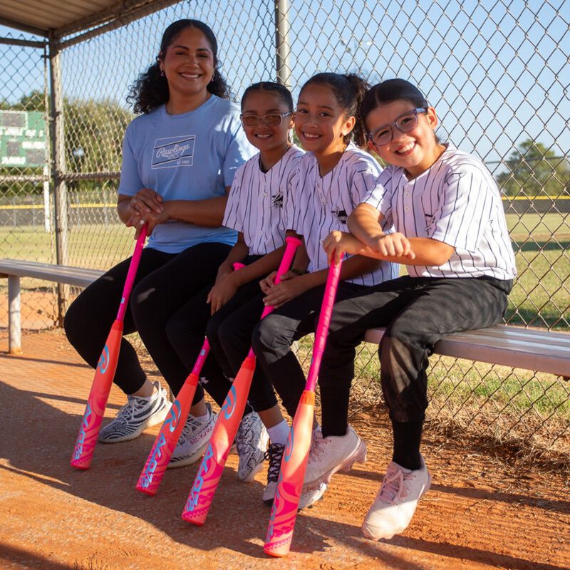 Picture of Jocelyn Alo and three young players sitting on a bench in a dugout with pink Rawlings ALO78 -12 fastpitch softball bats