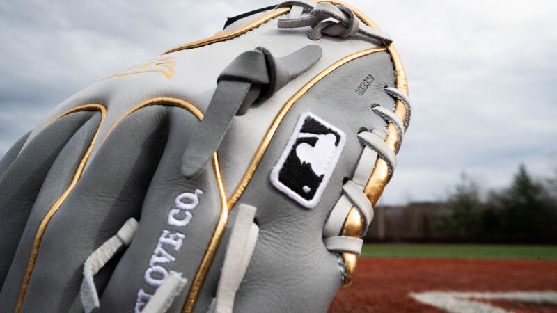 The MLB logo on the grey pinkie of a HOH exclusive infield glove on a field - SKU: PRO204W-2GW 
