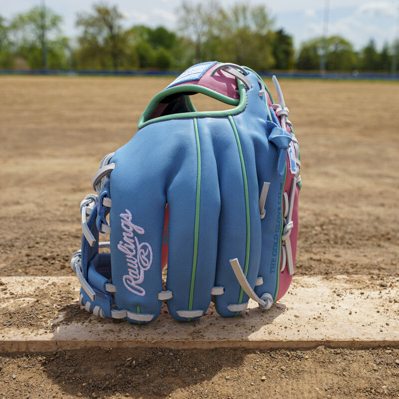 Picture of a columbia blue/pink Exclusive Rawlings NXT Series 11.5" Infield Glove standing on its fingertips on a pitching rubber