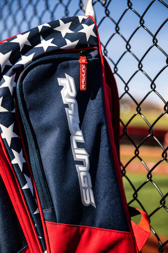 Side of a USA Rawlings Legion backpack on a fence with the Rawlings logo on the shoe compartment - SKU: LEGION-USA