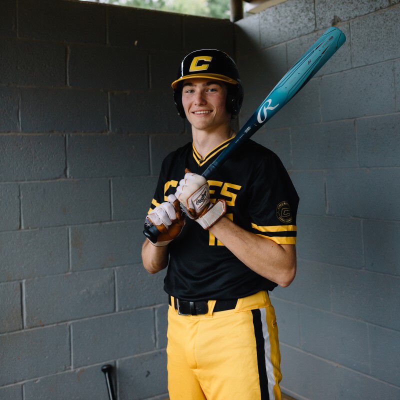 A player standing in the dugout holding a blue Clout AI baseball bat against his shoulder