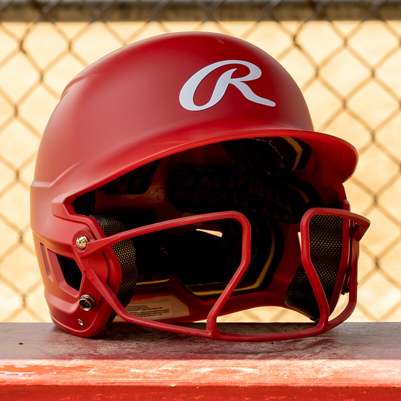 A red Mach hi-viz fastpitch helmet on a bench in a dugout - SKU: MCHVIZ
