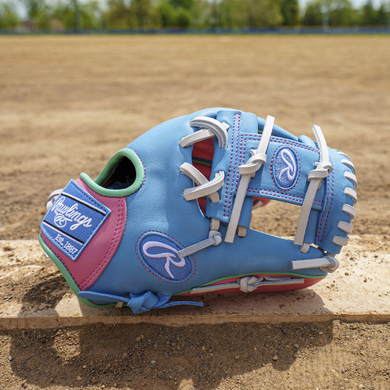 Picture of a columbia blue/pink Exclusive Rawlings NXT Series 11.5" Infield Glove on top of a pitching rubber