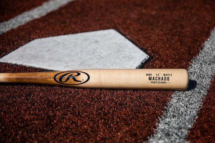 A natural wood colored Manny Machado wood bat lying at home plate - SKU: MM8PL
