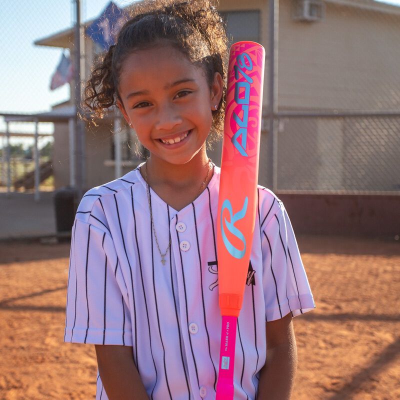 A girl holding a pink Rawlings ALO78 -12 fastpitch softball bat against her shoulder