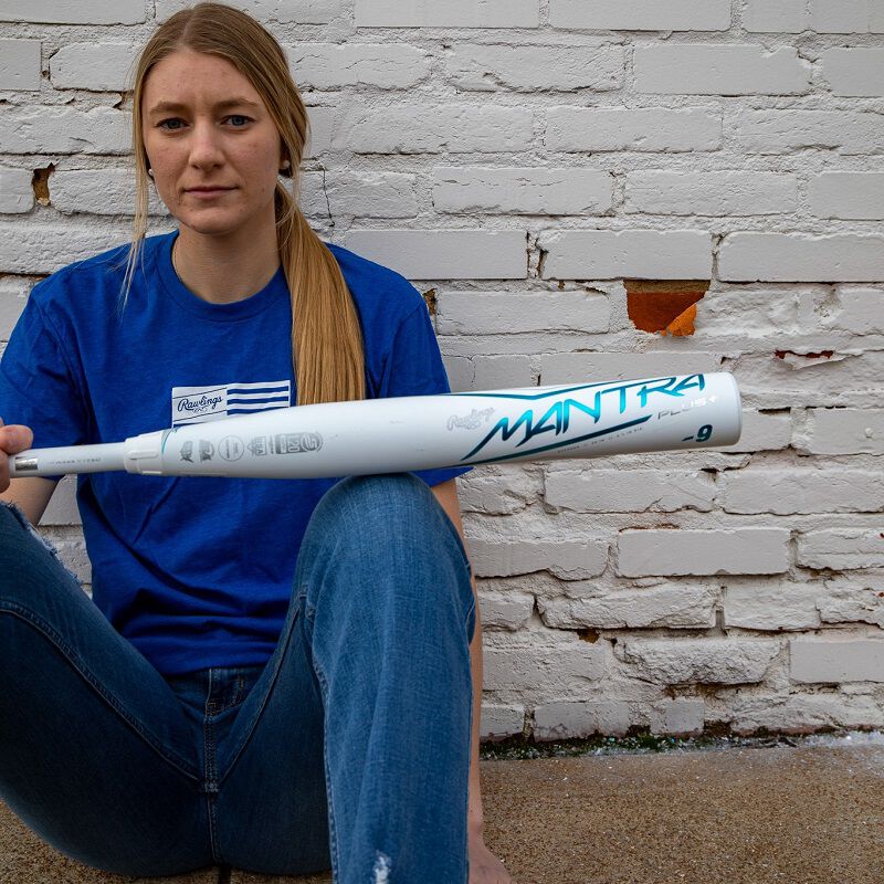 A player sitting down holding a white Rawlings Mantra+ fastpitch bat - SKU: RFP3MP