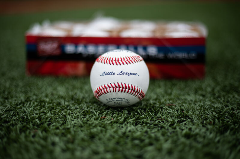A Rawlings Little League competition grade baseball lying on a field in front of a box of balls - SKU: RLLB1