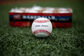 A Rawlings Little League competition grade baseball lying on a field in front of a box of balls - SKU: RLLB1 image number null